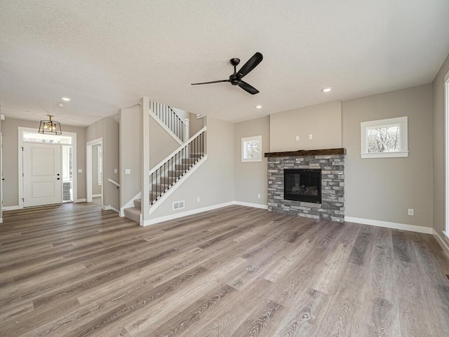 unfurnished living room featuring hardwood / wood-style flooring, ceiling fan, a stone fireplace, and a textured ceiling