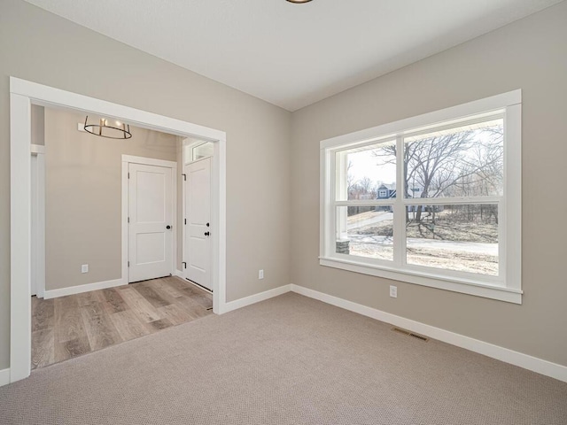 unfurnished room featuring light carpet and an inviting chandelier