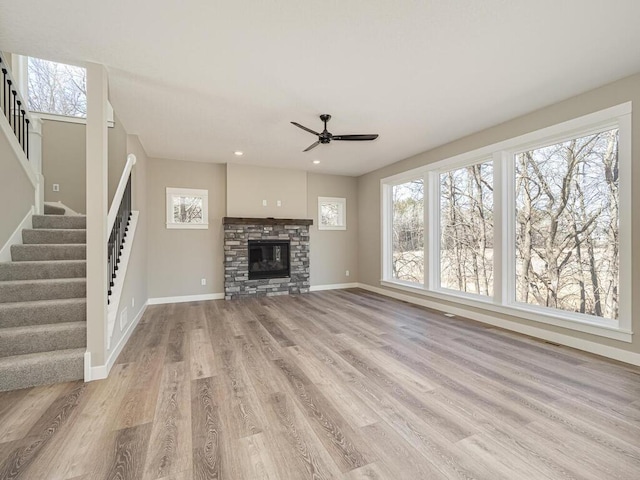 unfurnished living room with ceiling fan, a stone fireplace, and light wood-type flooring