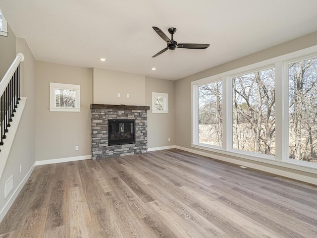 unfurnished living room with light hardwood / wood-style flooring, a stone fireplace, and ceiling fan