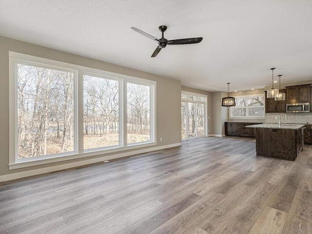 unfurnished living room with hardwood / wood-style floors, ceiling fan with notable chandelier, and sink