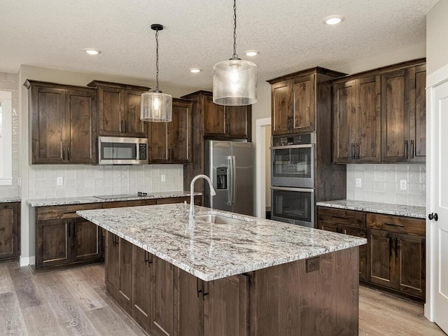 kitchen featuring pendant lighting, decorative backsplash, stainless steel appliances, and an island with sink