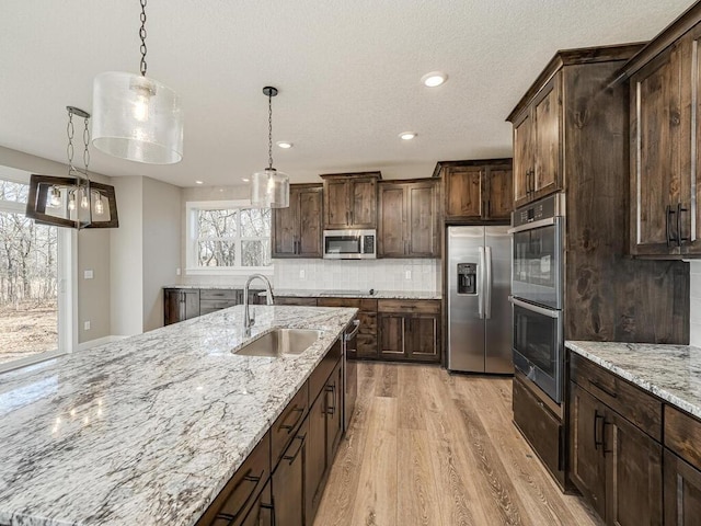 kitchen with sink, light stone counters, backsplash, pendant lighting, and appliances with stainless steel finishes