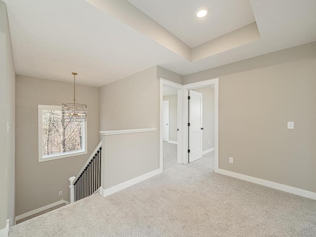 spare room with a raised ceiling, carpet floors, and a notable chandelier