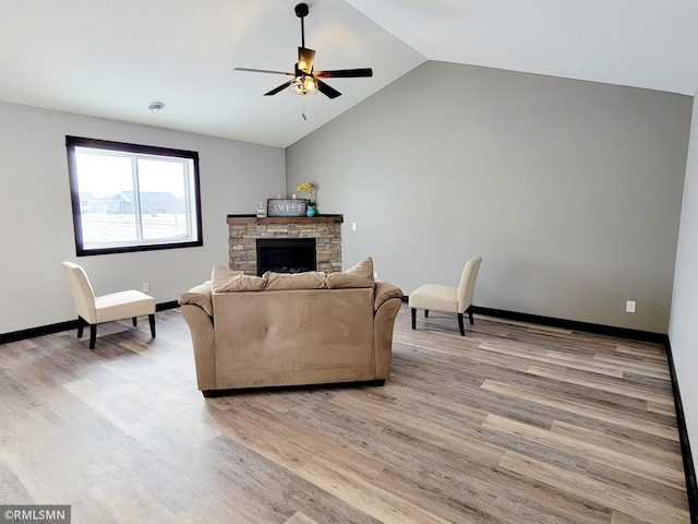 living room featuring vaulted ceiling, light hardwood / wood-style flooring, ceiling fan, and a stone fireplace