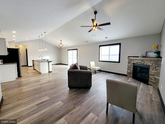 living room featuring lofted ceiling, sink, ceiling fan, light wood-type flooring, and a fireplace