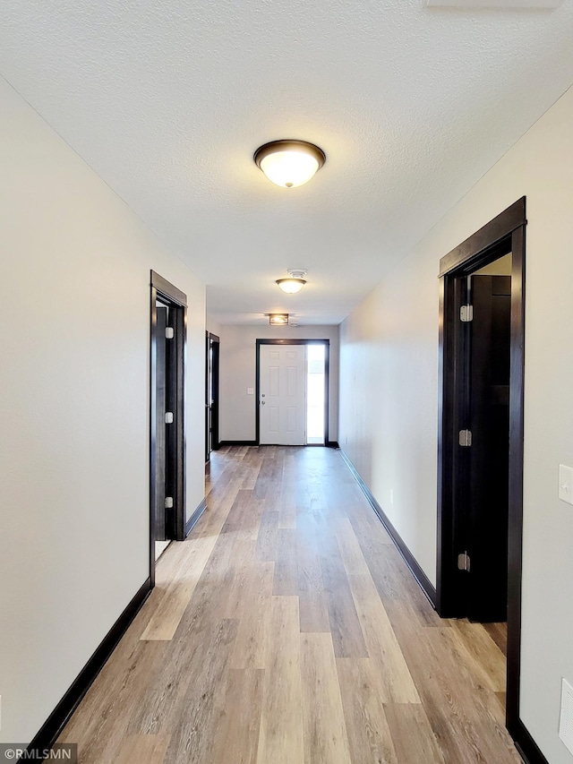 corridor featuring a textured ceiling and light hardwood / wood-style floors