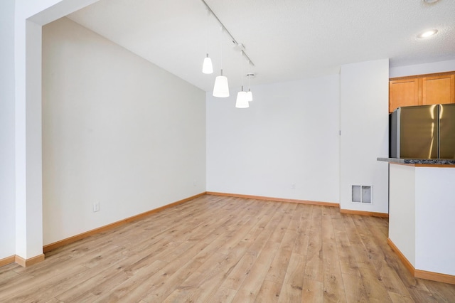 unfurnished dining area with track lighting, light hardwood / wood-style floors, and a textured ceiling