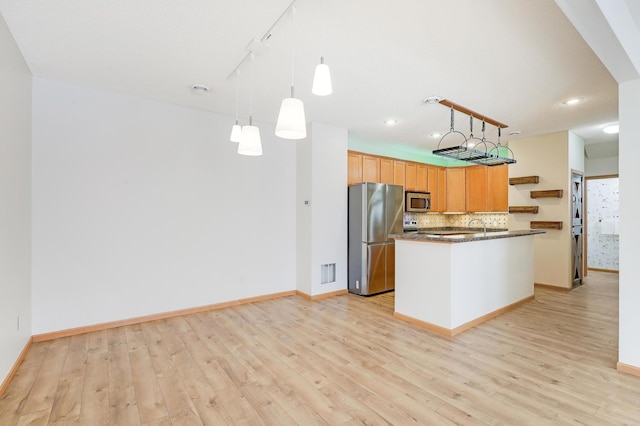 kitchen with pendant lighting, light hardwood / wood-style flooring, appliances with stainless steel finishes, tasteful backsplash, and a center island with sink