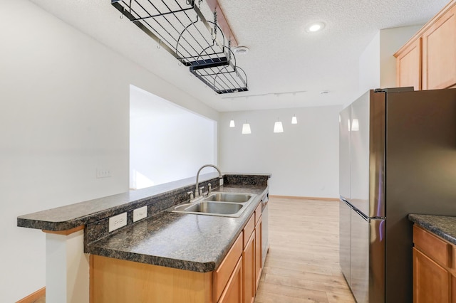 kitchen featuring sink, light hardwood / wood-style flooring, stainless steel refrigerator, a textured ceiling, and a center island with sink