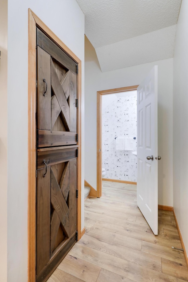 hallway featuring lofted ceiling, a textured ceiling, and light wood-type flooring