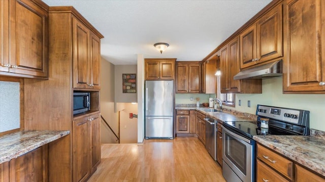 kitchen with light stone counters, sink, light wood-type flooring, and appliances with stainless steel finishes