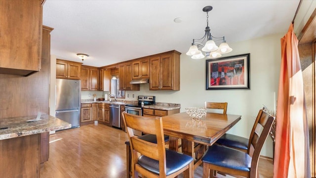 kitchen with light stone countertops, appliances with stainless steel finishes, a notable chandelier, light hardwood / wood-style floors, and hanging light fixtures