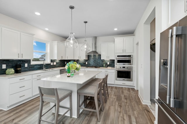 kitchen with white cabinets, sink, hanging light fixtures, wall chimney exhaust hood, and stainless steel appliances