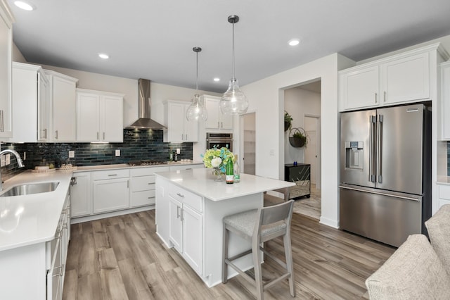 kitchen featuring white cabinets, stainless steel appliances, a kitchen island, and wall chimney range hood