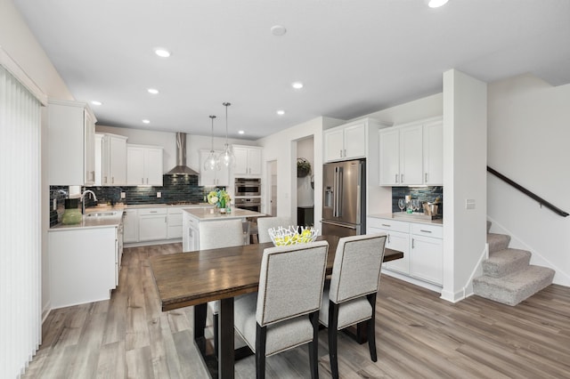 kitchen featuring sink, wall chimney exhaust hood, stainless steel appliances, decorative light fixtures, and a kitchen island