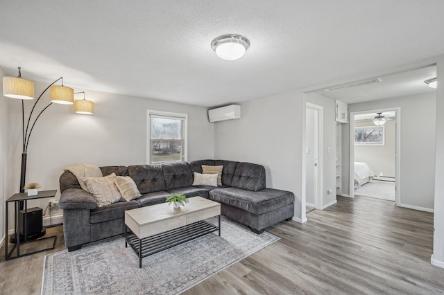 living room featuring ceiling fan, a wall mounted air conditioner, a baseboard heating unit, a textured ceiling, and hardwood / wood-style flooring