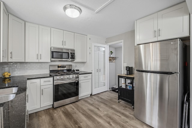 kitchen featuring appliances with stainless steel finishes, dark stone countertops, backsplash, a textured ceiling, and white cabinets