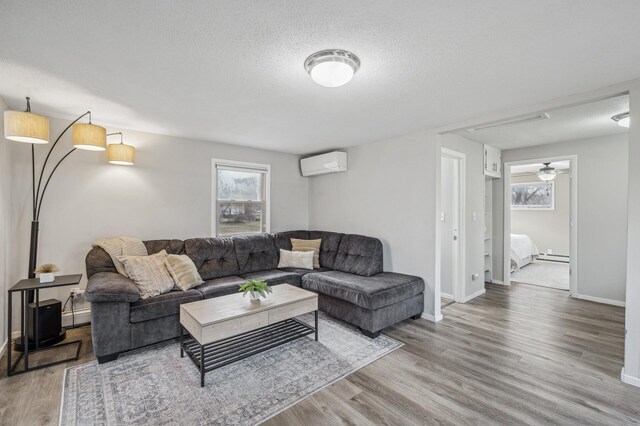 living room featuring a wall mounted air conditioner, wood-type flooring, a textured ceiling, baseboard heating, and ceiling fan