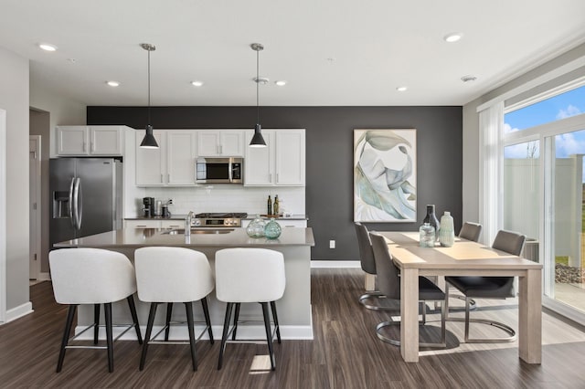 kitchen featuring a center island with sink, appliances with stainless steel finishes, tasteful backsplash, decorative light fixtures, and white cabinetry