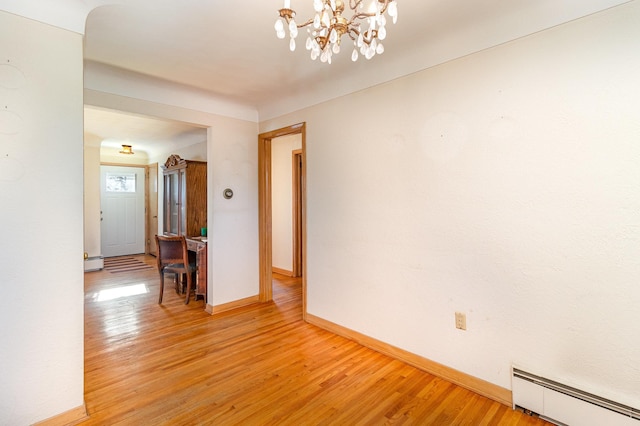 spare room featuring an inviting chandelier, a baseboard heating unit, and hardwood / wood-style flooring