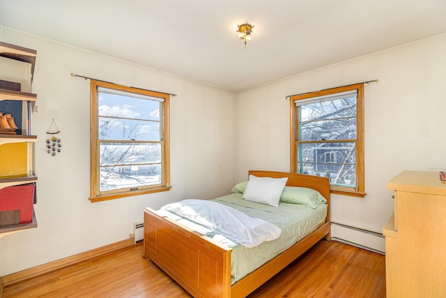 bedroom featuring baseboard heating, light hardwood / wood-style floors, and multiple windows