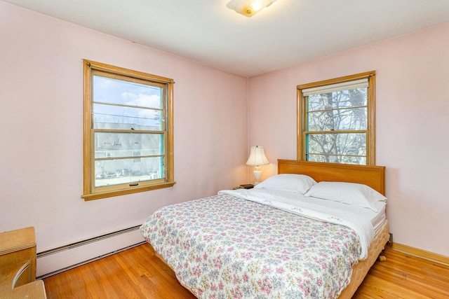 bedroom with a baseboard heating unit and light hardwood / wood-style flooring