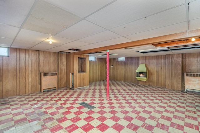 basement featuring radiator heating unit, wooden walls, and a paneled ceiling