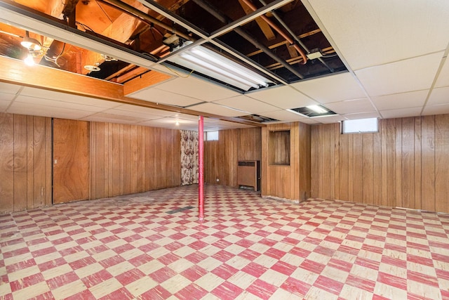 basement with a drop ceiling and wood walls