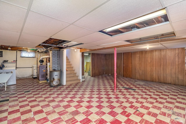 basement with water heater, a paneled ceiling, and wooden walls