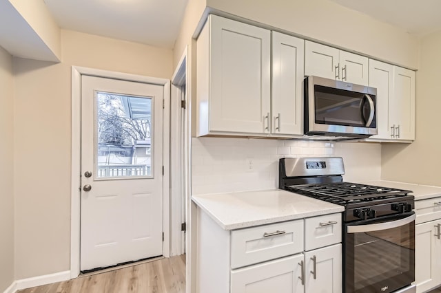 kitchen with white cabinets, light stone countertops, light hardwood / wood-style flooring, and gas stove