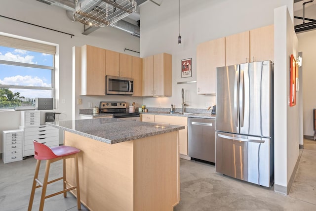 kitchen with dark stone counters, stainless steel appliances, sink, light brown cabinets, and a kitchen island