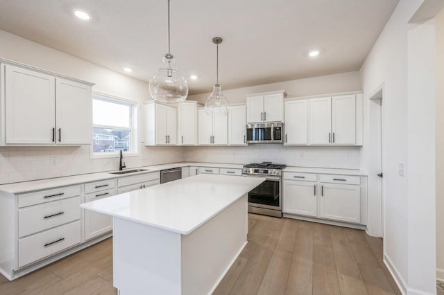 kitchen featuring sink, appliances with stainless steel finishes, a center island, white cabinets, and decorative light fixtures