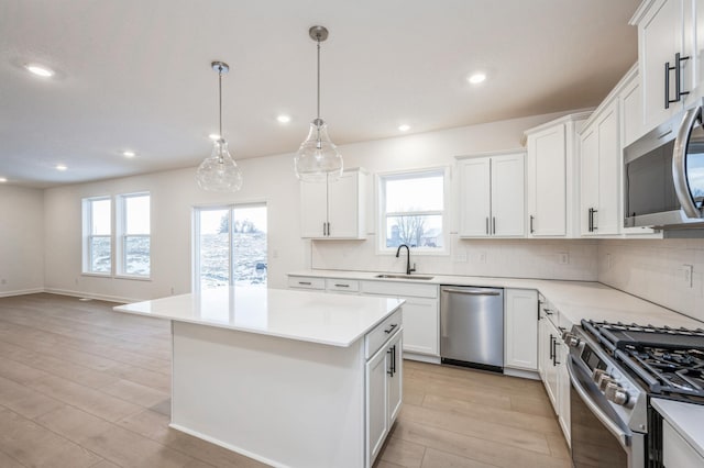 kitchen featuring sink, hanging light fixtures, stainless steel appliances, white cabinets, and a kitchen island