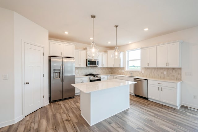 kitchen with a center island, sink, hanging light fixtures, white cabinetry, and stainless steel appliances