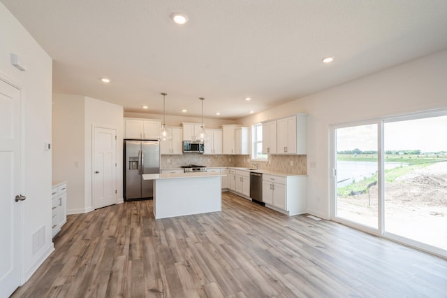 kitchen with a center island, white cabinets, decorative light fixtures, and appliances with stainless steel finishes