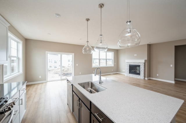 kitchen featuring light stone countertops, stainless steel dishwasher, a stone fireplace, and sink