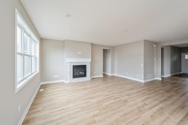 unfurnished living room with a stone fireplace and light wood-type flooring