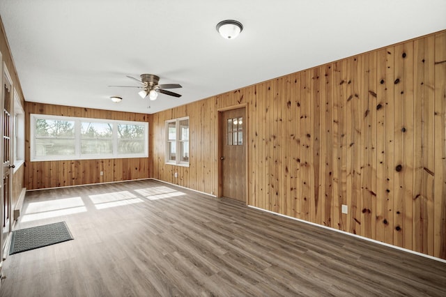 spare room with hardwood / wood-style floors, wooden walls, and ceiling fan