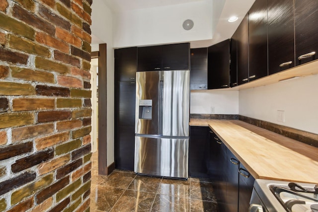 kitchen featuring wood counters, stove, stainless steel fridge with ice dispenser, and brick wall