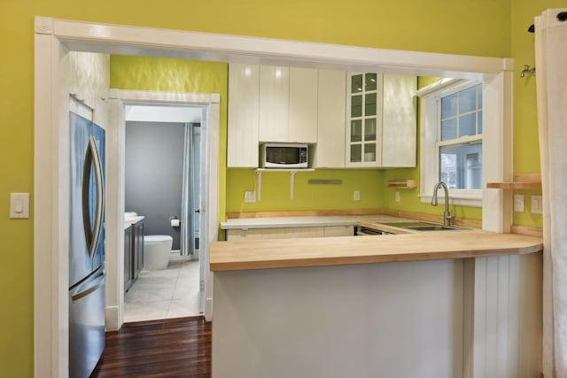 kitchen with kitchen peninsula, white cabinetry, sink, and stainless steel refrigerator