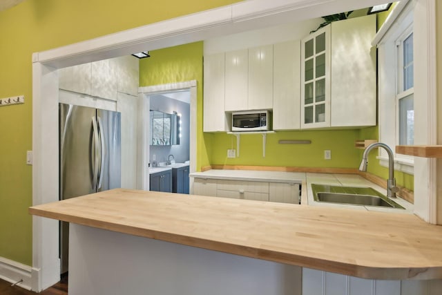 kitchen featuring white cabinets, sink, stainless steel refrigerator, and wooden counters