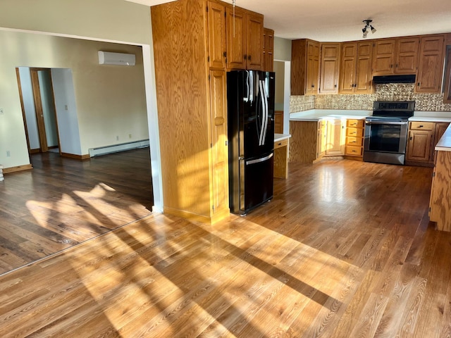 kitchen with electric range, brown cabinets, freestanding refrigerator, light countertops, and under cabinet range hood