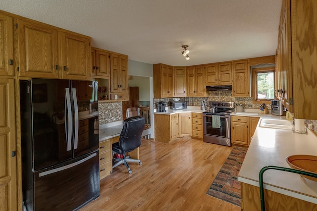 kitchen with under cabinet range hood, light wood-style floors, light countertops, stainless steel electric range, and freestanding refrigerator