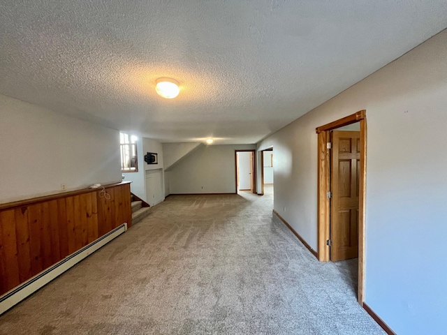 unfurnished room featuring baseboard heating, light carpet, a textured ceiling, baseboards, and stairs