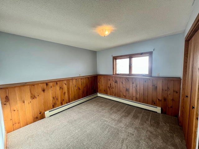 carpeted spare room with a baseboard heating unit, wainscoting, a textured ceiling, and wooden walls