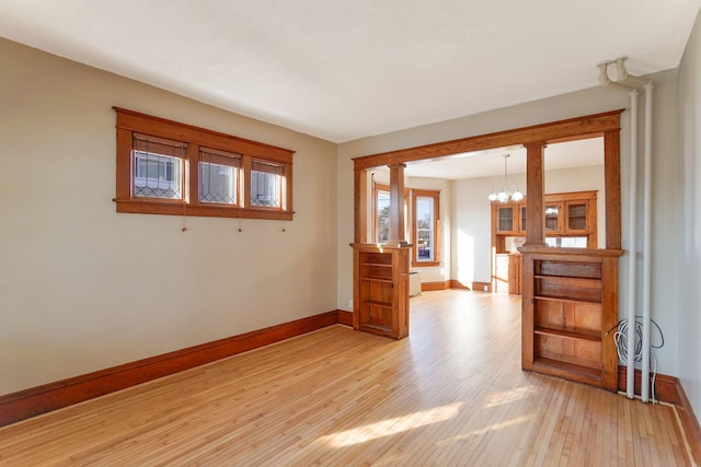 unfurnished room featuring ornate columns, light wood-type flooring, and a notable chandelier