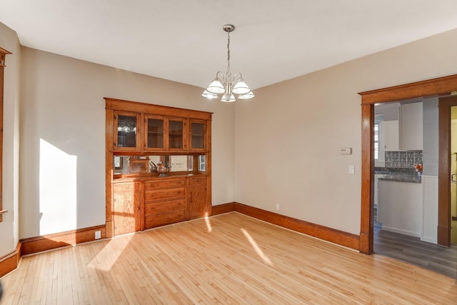 unfurnished dining area with an inviting chandelier and light wood-type flooring