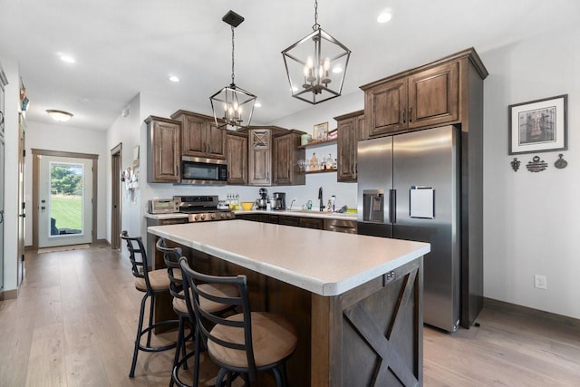 kitchen with dark brown cabinets, a kitchen island, light wood-type flooring, and appliances with stainless steel finishes