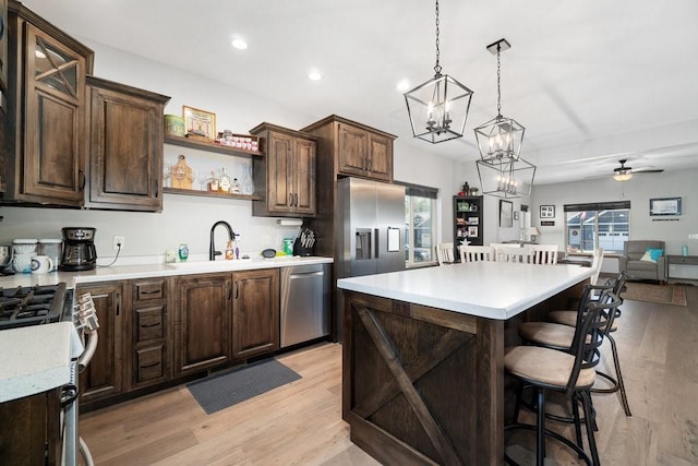 kitchen featuring a center island, stainless steel appliances, pendant lighting, dark brown cabinets, and ceiling fan with notable chandelier